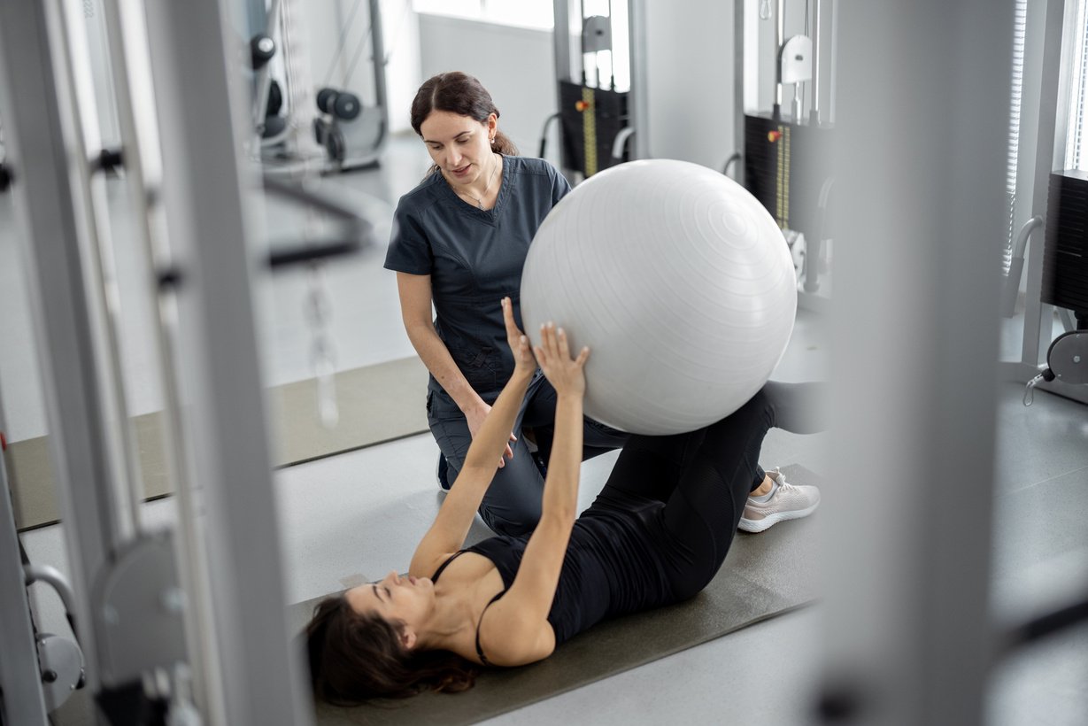 Physiotherapist Assisting Woman Exercising with Fitness Ball